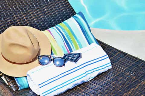 Beach lounger with striped towel, straw hat, and sunglasses by a bright blue swimming pool