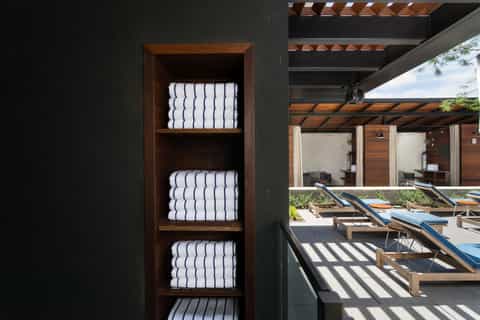 Wooden shelf with stacked white towels next to pool deck with loungers and pergola
