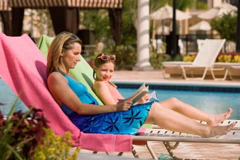 Woman and child relaxing on colorful loungers by resort pool, reading magazine