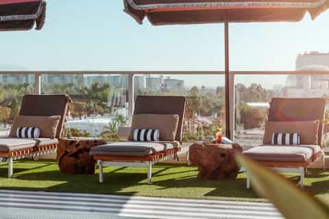 Rooftop lounge with chaise lounges, striped cushions, and city skyline views under brown umbrellas