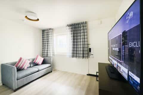 Modern living room with gray sofa, pink striped pillows, checkered curtains, and wall-mounted TV