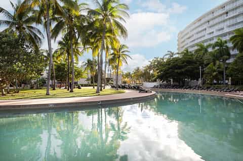 Resort pool with palm trees, lounge chairs, and curved walkway beside multi-story building