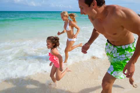 Family running together on a sandy beach in turquoise water on a sunny day