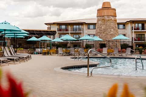 Resort pool area with turquoise umbrellas, lounge chairs, and multi-story hotel building with stone tower