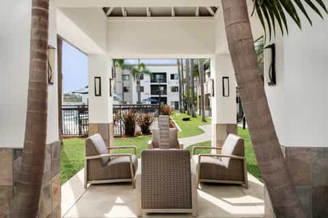 Covered patio with rattan lounge chairs overlooking a resort courtyard with palm trees and green lawn