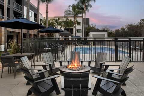 Outdoor firepit lounge with Adirondack chairs, umbrellas, and pool view at dusk