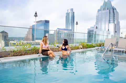 Woman in pool overlooking city skyline with modern skyscrapers and urban landscape