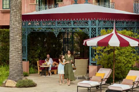 Elegant courtyard with ornate cast iron pergola, red and white striped umbrella, lounge seating, and palm tree accents