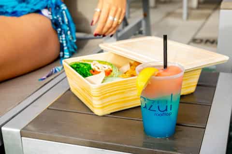 Colorful layered beverage and food container poolside at resort with person's hand visible