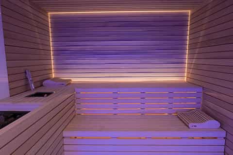 Modern sauna interior with wooden benches and glowing neon orange and blue lighting strips