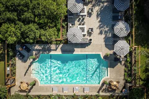 Overhead view of resort pool with striped umbrellas, loungers, and surrounding patio surrounded by greenery