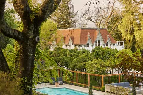 Elegant white manor with terracotta roof nestled among tall trees, view from pool area with wooden deck