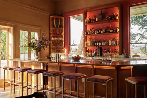 Upscale home bar with orange-lit shelving displaying spirits bottles, wooden counter, and purple bar stools