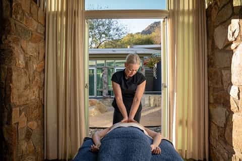 Massage therapist performing treatment on client in stone spa room with mountain views