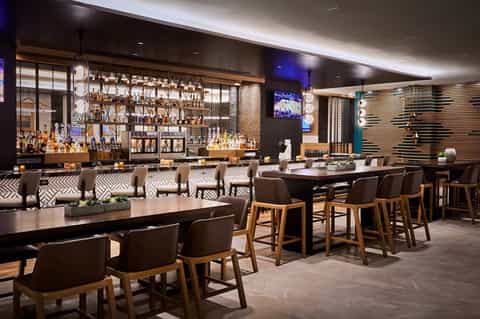 Modern hotel bar with geometric patterned seating, illuminated shelving, and dark contemporary design