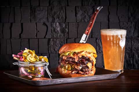 Gourmet burger with caramelized onions, pickles, fries, and craft beer on dark slate background