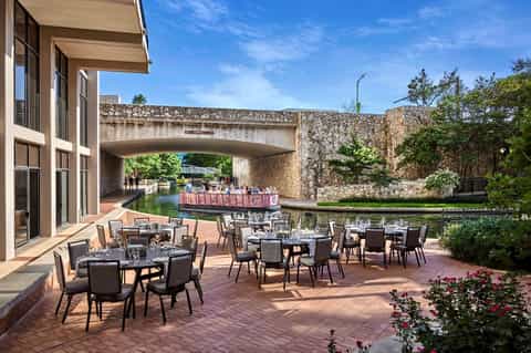 Outdoor dining terrace beside a canal with stone bridges and manicured gardens