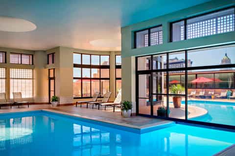 Indoor swimming pool with large windows overlooking an outdoor pool and city skyline