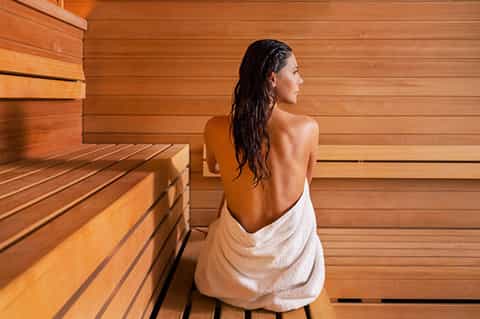 Woman in sauna with wet hair sitting on wooden bench in cedar-lined sauna room