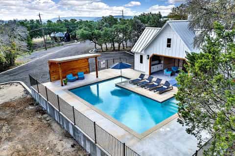 Modern poolside resort with turquoise lap pool, white cabana, lounge chairs, and surrounding oak trees on rural property