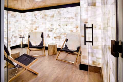 Spa relaxation room with cream chairs, white stone walls, wooden ceiling, and minimalist décor