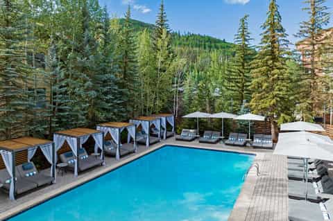 Resort pool with cabanas surrounded by evergreen forest and mountains under clear sky