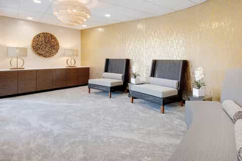 Modern hotel lobby with gold textured walls, wooden reception desk, and contemporary seating areas with neutral upholstery