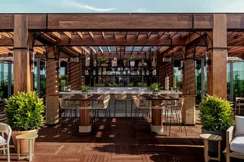 Outdoor rooftop bar with wooden pergola, terrace seating, and mountain views
