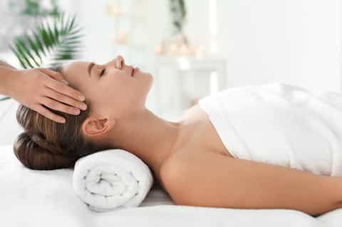 Woman receiving head massage at spa with white towels and green plants in background