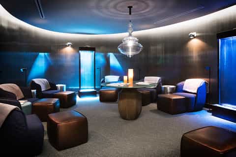 Modern circular lounge with blue ambient lighting, brown leather ottomans, glass pendant light, and contemporary furnishings