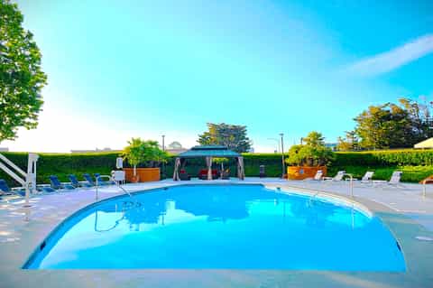Resort swimming pool with clear blue water, lounge chairs, and cabana pavilion under bright sunny sky