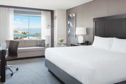 Luxury hotel room with floor-to-ceiling windows overlooking a bay and coastal cityscape