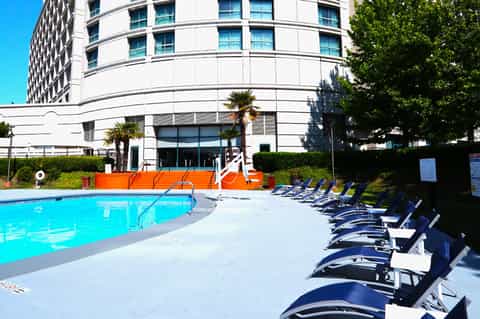 Outdoor resort pool with turquoise water, lounge chairs, and curved modern white building with palm trees