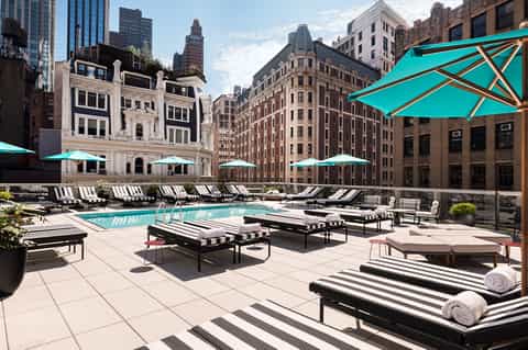 Rooftop pool deck with turquoise umbrellas, striped loungers, and historic buildings in urban skyline backdrop