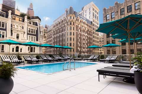 Rooftop pool with turquoise umbrellas and loungers overlooking historic downtown buildings