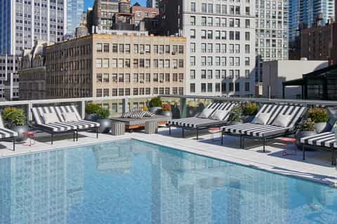 Rooftop pool with striped loungers overlooking Manhattan skyline and city buildings