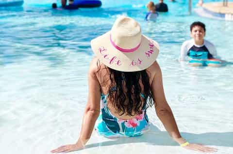 Woman in white sun hat wading in shallow turquoise water at a beach resort