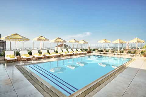 Rooftop pool with yellow striped umbrellas, lounge chairs, and city skyline views