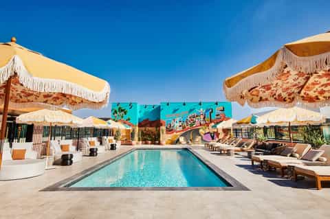 Retro-styled resort pool with yellow umbrellas, lounge chairs, and vintage signage under clear blue sky