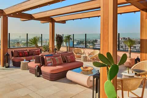 Rooftop terrace with wooden pergola, burgundy seating, and panoramic city skyline views