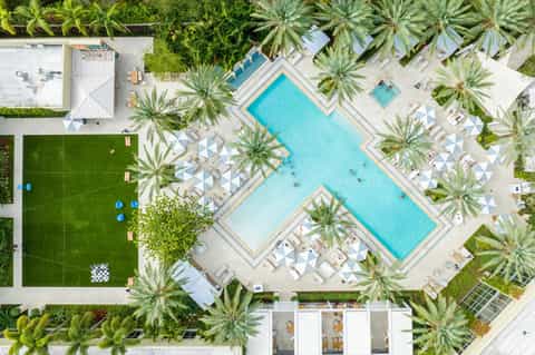 Aerial view of resort with two turquoise pools, palm trees, lounge chairs, and white umbrellas