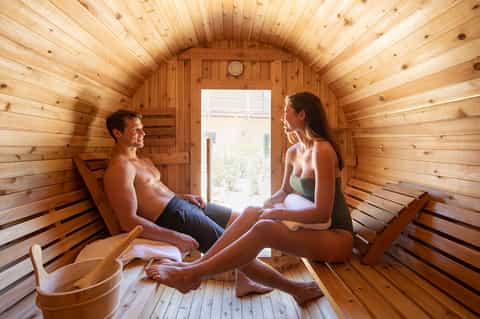 Couple relaxing in a wooden sauna with light streaming through the door