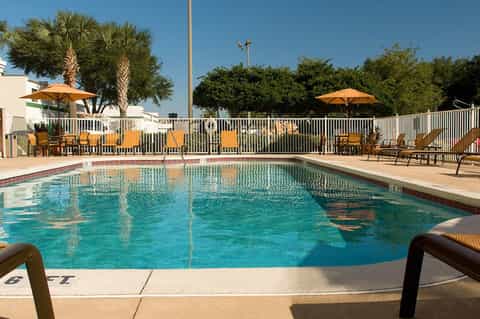 Resort swimming pool with turquoise water, yellow umbrellas, lounge chairs, and palm trees under clear sky
