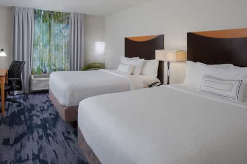 Modern hotel room with two queen beds, dark headboards, white bedding, and large windows with nature views