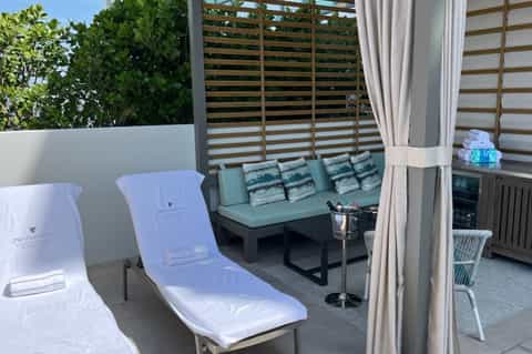 Luxury spa terrace with white lounge chairs, green cushioned seating, wooden privacy screens, and lush greenery