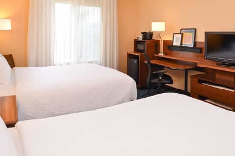 Hotel room with two queen beds, orange walls, work desk with TV, and natural light from sliding glass doors
