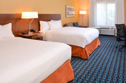 Hotel room with two queen beds, orange accents, wood headboards, and patterned blue carpet