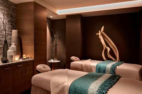 Luxury spa treatment room with dual massage beds, wooden sculptural art, and warm ambient lighting
