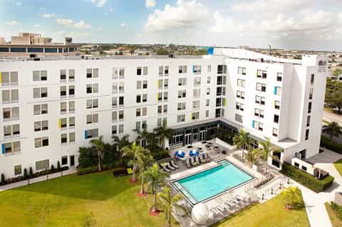 Modern white hotel building with central courtyard pool, palm trees, and lounge seating