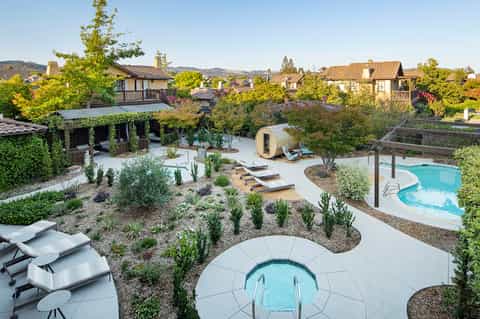 Aerial view of luxury resort with multiple pools, spa cabins, loungers, and villa-style homes nestled in hills